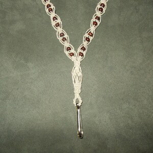 May include: A white macrame cord necklace with brown wooden beads and a silver metal clasp.
