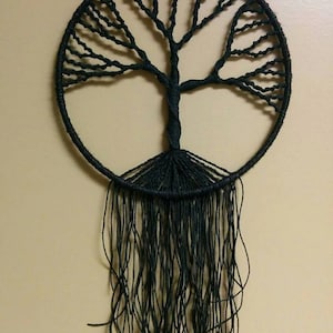 May include: A black macrame wall hanging in the shape of a tree with long strands hanging down.