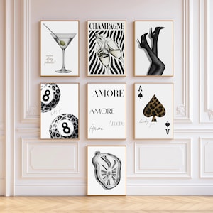 Op de afbeelding: Een galerijwandset van zeven ingelijste kunstprints met zwart-wit illustraties. De ontwerpen bevatten een martiniglas, champagneglazen op zebrastreeppatroon, benen op hakken, achtballen met luipaardprint, het woord Amore, een schoppenaas en een smeltende klok.