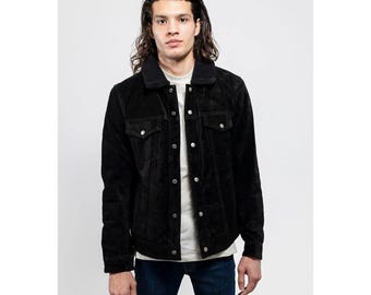 May include: Black corduroy jacket with a black faux fur collar. The jacket has two chest pockets and two side pockets. It is buttoned up and worn over a light gray t-shirt and dark blue jeans.