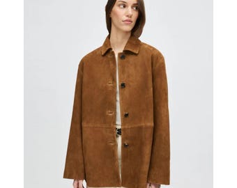 May include: A brown suede jacket with a button-up front and a collared neckline. The jacket has long sleeves and a relaxed fit. The color is a warm, earthy brown, and the material appears soft and textured. The jacket is a classic outerwear piece.