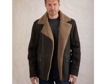 May include: A brown shearling jacket with a tan shearling collar and lining. The jacket has a zip closure, two front pockets, and a classic aviator style. The model is wearing a dark gray t-shirt and blue jeans.