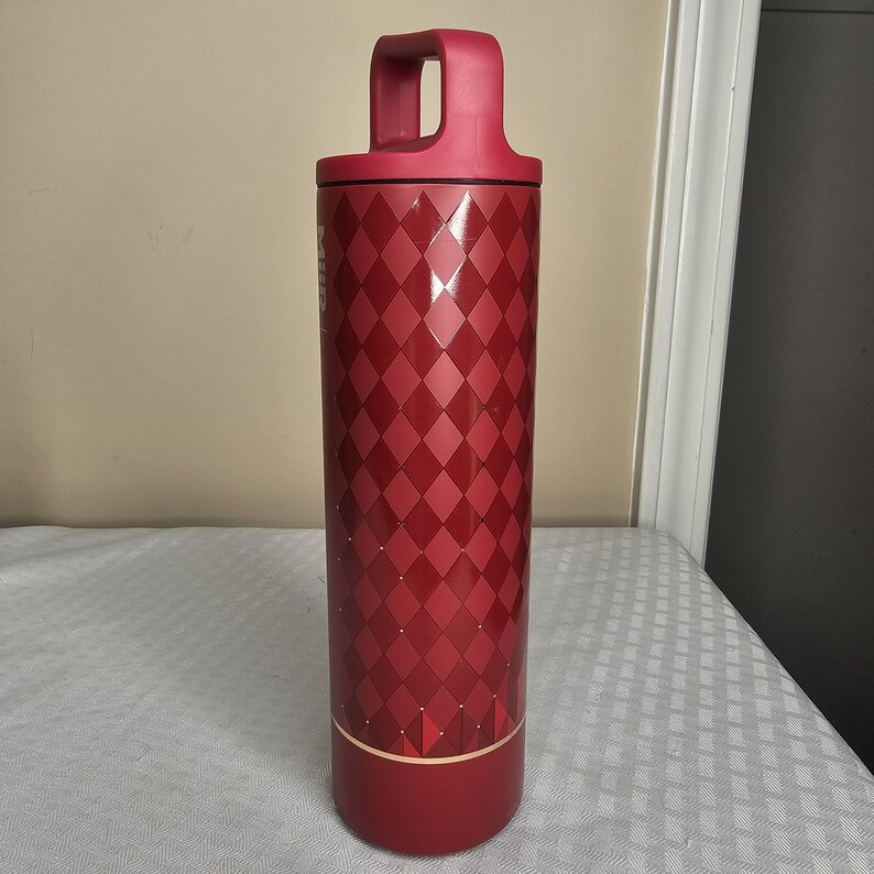 K&ouml;nnte beinhalten: Eine hohe, rote isolierte Wasserflasche mit Griff. Die Flasche hat ein Rautenmuster in verschiedenen Rott&ouml;nen. Der Griff und der Boden sind ein durchgehendes, dunkleres Rot. Die Flasche ist so konzipiert, dass sie Getr&auml;nke kalt oder hei&szlig; h&auml;lt.
