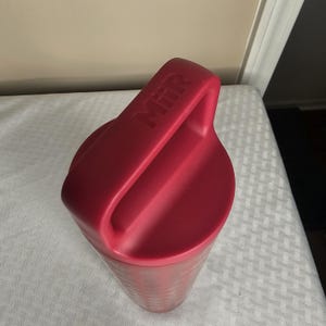 K&ouml;nnte beinhalten: Ein roter Isolierbecher mit Griff. Der Becher hat eine strukturierte Oberfl&auml;che und der Markenname "MiiR" ist auf dem Griff eingepr&auml;gt. Der Becher ist so konzipiert, dass Getr&auml;nke &uuml;ber einen l&auml;ngeren Zeitraum hei&szlig; oder kalt gehalten werden.