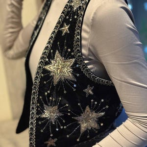 K&ouml;nnte beinhalten: Schwarze Samtweste mit silbernen und goldenen Sternen und Pailletten verziert. Die Weste hat eine dekorative Bord&uuml;re an den R&auml;ndern. &Auml;rmellos und mit V-Ausschnitt. Ein einzigartiges Modeaccessoire.