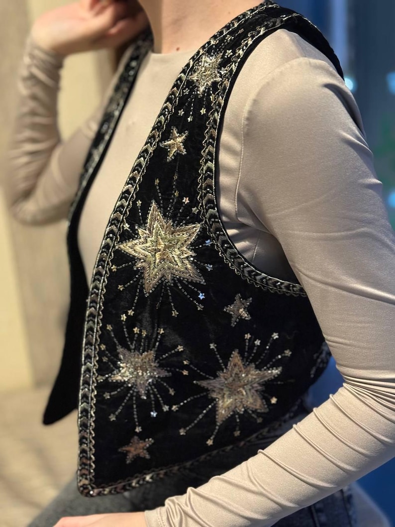 K&ouml;nnte beinhalten: Schwarze Samtweste mit silbernen und goldenen Sternen und Pailletten verziert. Die Weste hat eine dekorative Bord&uuml;re an den R&auml;ndern. &Auml;rmellos und mit V-Ausschnitt. Ein einzigartiges Modeaccessoire.