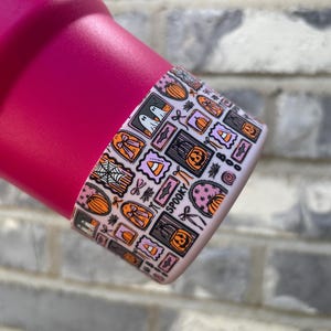 May include: A magenta-colored tumbler with a decorative band featuring Halloween-themed illustrations. The band includes images of ghosts, pumpkins, spiderwebs, and the word "Spooky" in a playful font. The design incorporates orange, black, and purple colors.