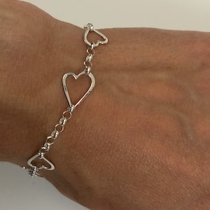 May include: A silver bracelet with a chain link design and four open heart charms.