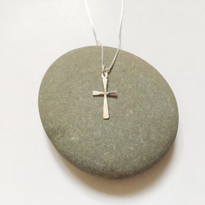 Puede incluir: Un collar de cadena de plata con un simple colgante de cruz de plata.