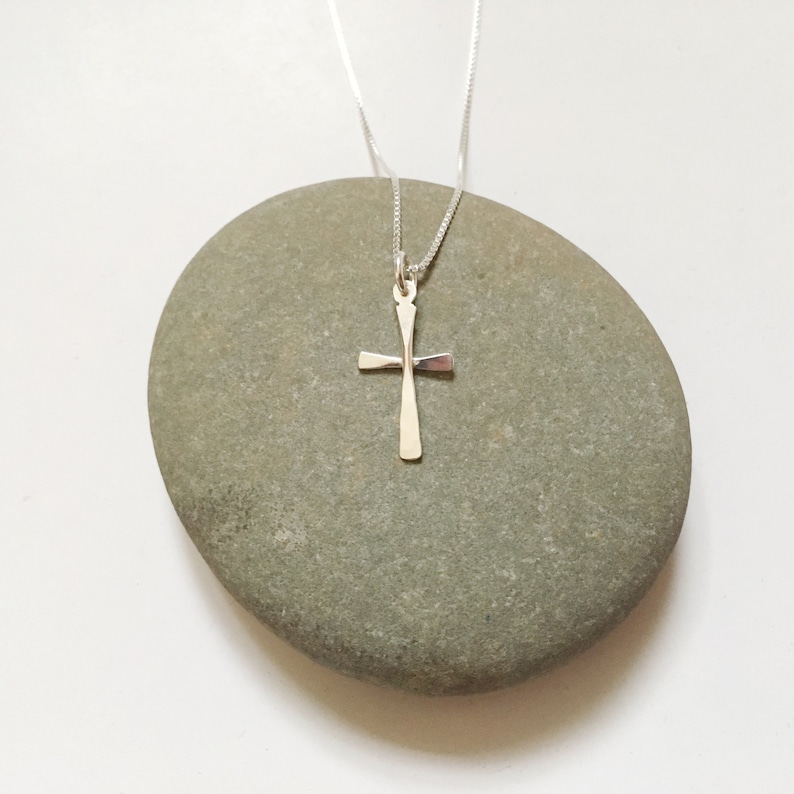 Puede incluir: Un collar de cadena de plata con un simple colgante de cruz de plata.