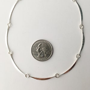 May include: A silver necklace with a hammered finish and a curved design. The necklace is about the size of a quarter.