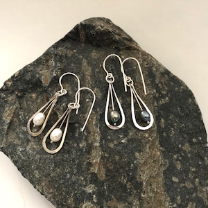 May include: Two pairs of silver dangle earrings with a pearl drop. One pair has a white pearl and the other has a black pearl.