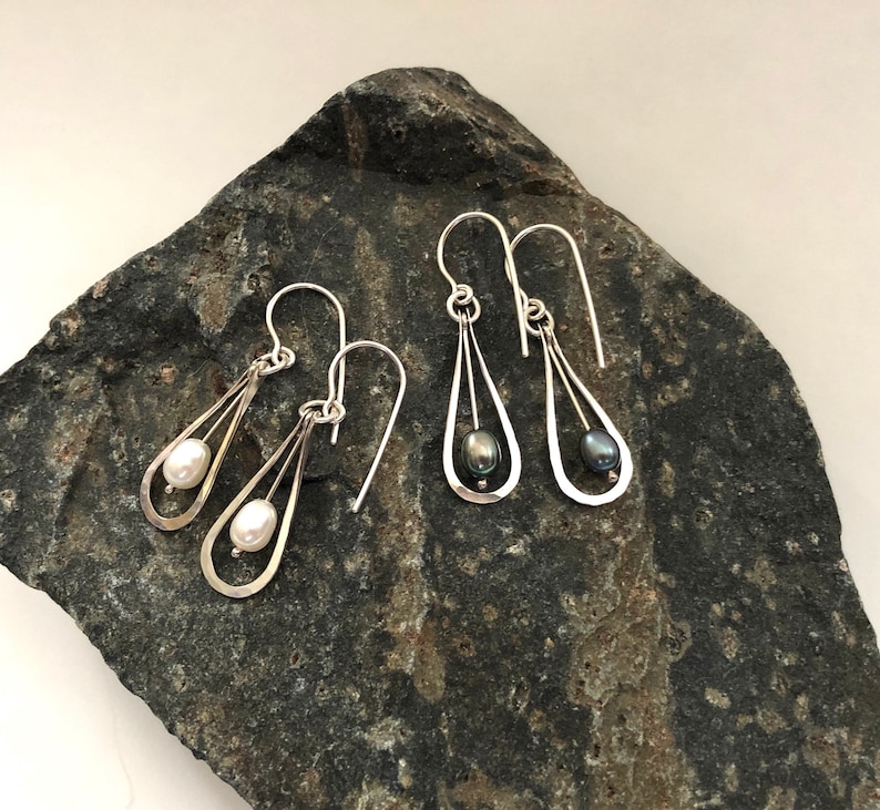May include: Two pairs of silver dangle earrings with a pearl drop. One pair has a white pearl and the other has a black pearl.