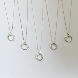 May include: Five silver necklaces with a pendant of interlocking rings. Each necklace has a delicate chain.