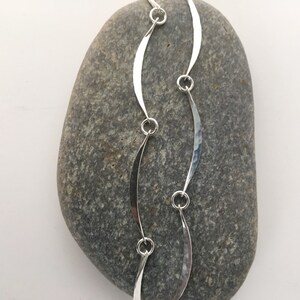 May include: A silver chain necklace with a wavy, hammered design. The chain is made of multiple connected links, each with a curved shape.