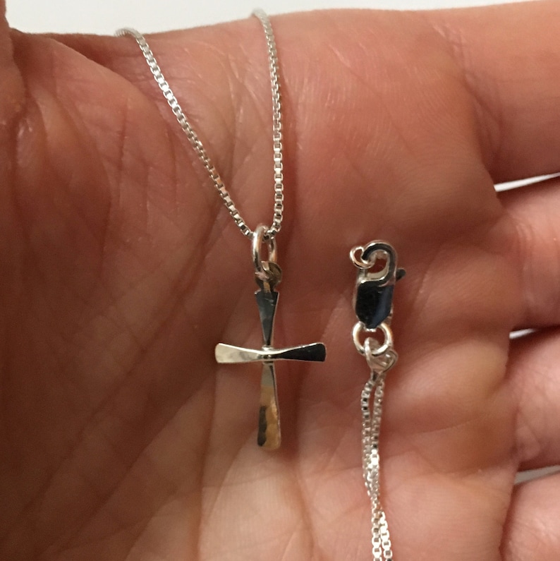 Puede incluir: Un collar de cadena de plata con un peque&ntilde;o colgante de cruz de plata. La cadena es de estilo cadena de caja.