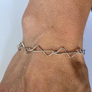May include: A silver-toned bracelet featuring a series of interconnected triangular wire links. The chain is constructed from thin, polished metal segments that form a repeating geometric pattern around the wrist, creating a delicate and continuous link design.