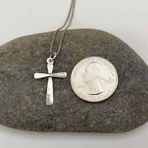 Puede incluir: Un collar de cadena de plata con un colgante de cruz de plata martillada. El colgante es aproximadamente del tama&ntilde;o de una moneda de 25 centavos de d&oacute;lar estadounidense.