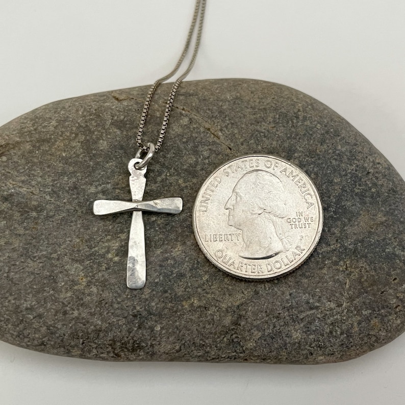 Puede incluir: Un collar de cadena de plata con un colgante de cruz de plata martillada. El colgante es aproximadamente del tama&ntilde;o de una moneda de 25 centavos de d&oacute;lar estadounidense.
