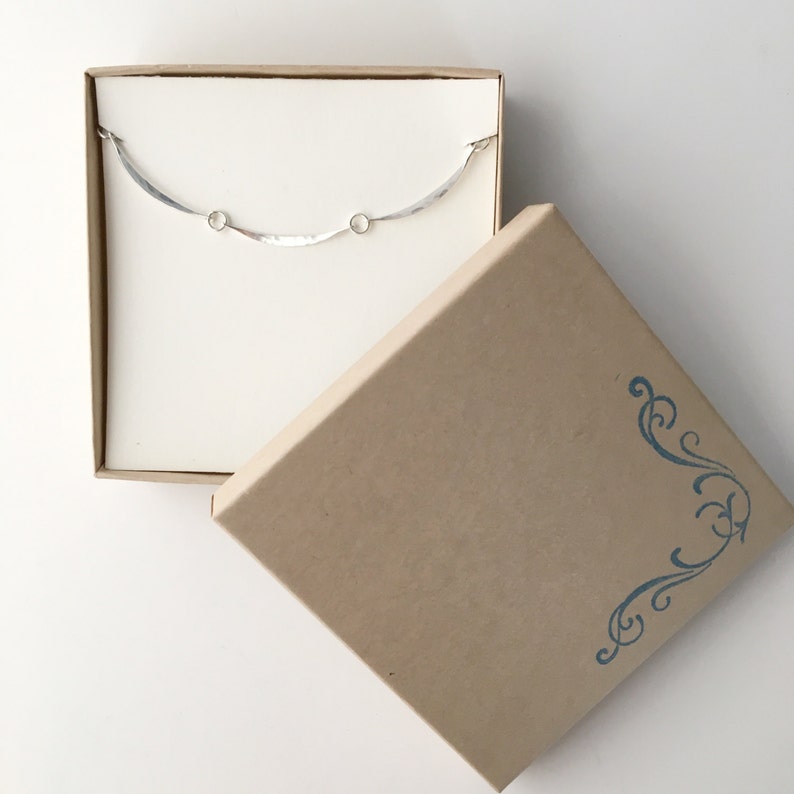 May include: A silver necklace with a wavy design and two small circles. The necklace is in a brown box with a blue floral design.