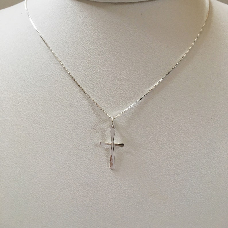 Puede incluir: Un collar de cadena de plata con un peque&ntilde;o colgante de cruz de plata.