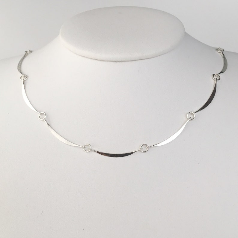 May include: A silver necklace with a curved, flat chain and small round links.