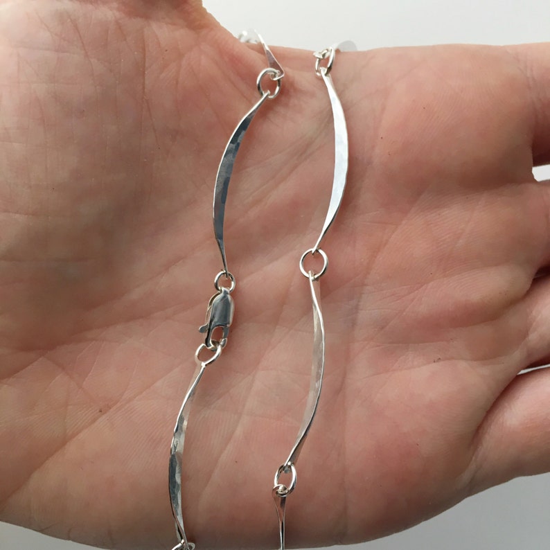 May include: A silver chain necklace with a hammered finish and a curved link design.