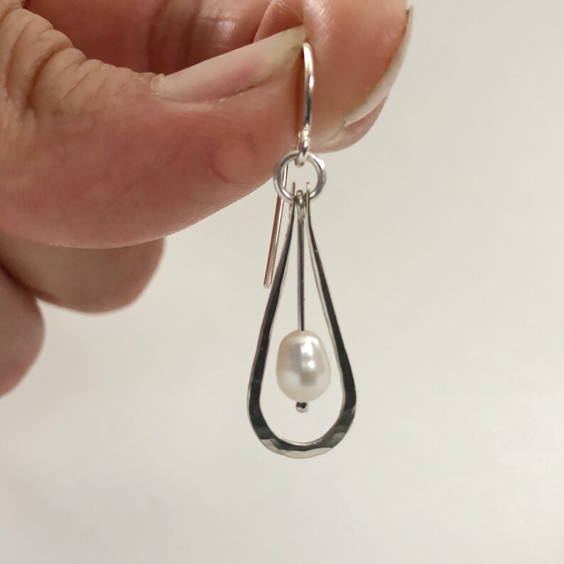 May include: Silver teardrop shaped earrings with a single white pearl hanging from the bottom.