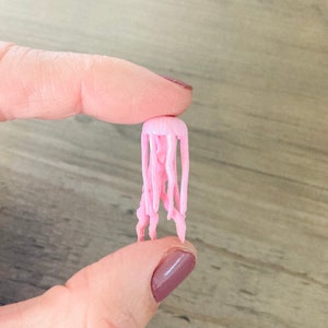 May include: A small pink plastic jellyfish figurine with a round head and long, thin tentacles.