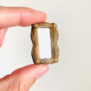 May include: A small, ornate gold-colored metal picture frame with a clear glass insert.