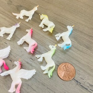Peut inclure: Une collection de huit petites figurines de licorne iris&eacute;es avec des ailes et des cornes. Les figurines sont en plastique et peintes dans diff&eacute;rentes couleurs pastel, notamment le rose, le bleu, le jaune et le vert. Les figurines sont dispos&eacute;es en cercle sur une surface en bois.
