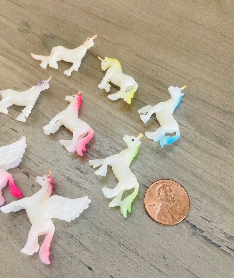 Peut inclure: Une collection de huit petites figurines de licorne iris&eacute;es avec des ailes et des cornes. Les figurines sont en plastique et peintes dans diff&eacute;rentes couleurs pastel, notamment le rose, le bleu, le jaune et le vert. Les figurines sont dispos&eacute;es en cercle sur une surface en bois.