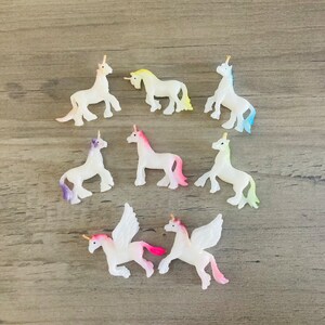 Peut inclure: Une collection de dix petites figurines de licorne blanches avec des ailes et des cornes iris&eacute;es. Les licornes sont dans diff&eacute;rentes poses, certaines debout, certaines courant et certaines volant.
