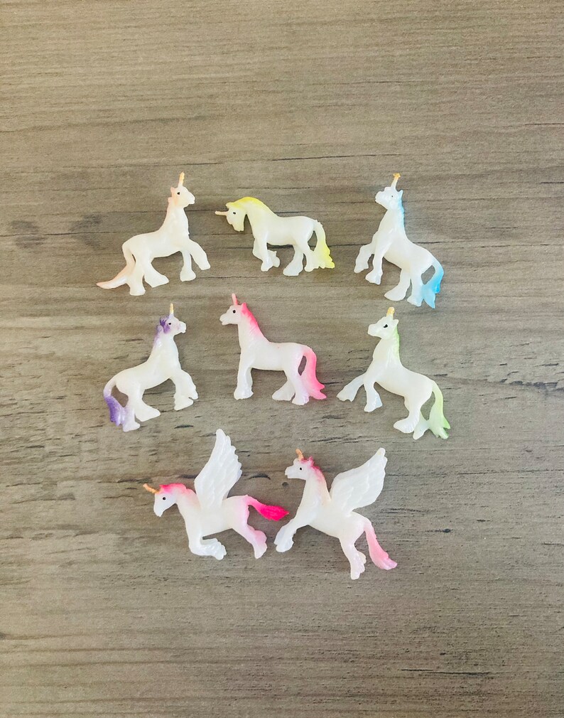 Peut inclure: Une collection de dix petites figurines de licorne blanches avec des ailes et des cornes iris&eacute;es. Les licornes sont dans diff&eacute;rentes poses, certaines debout, certaines courant et certaines volant.