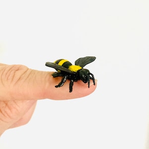 May include: A small black and yellow plastic bee toy. The bee has black wings and yellow stripes on its body.