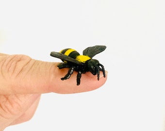 May include: A small black and yellow plastic bee toy. The bee has black wings and yellow stripes on its body.