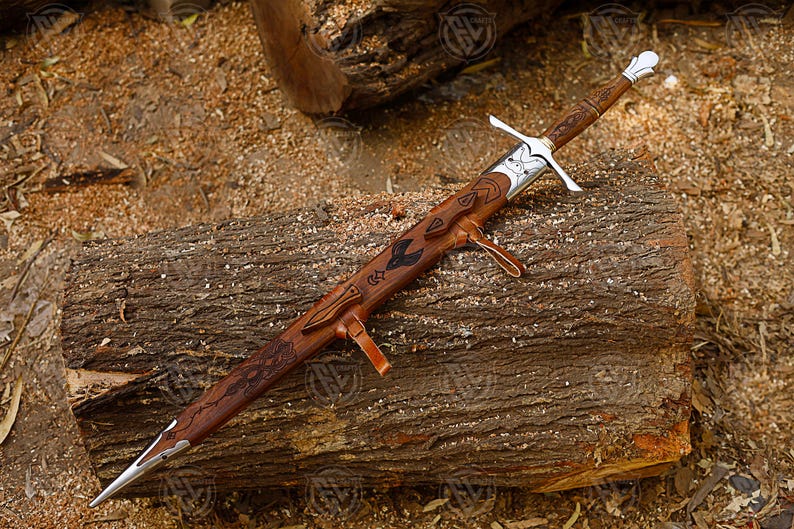 Puede incluir: Una espada artesanal con empu&ntilde;adura y vaina de madera marr&oacute;n, apoyada sobre un tronco de madera. La espada presenta una guarda plateada y un dise&ntilde;o detallado en la vaina. La hoja es plateada y puntiaguda.
