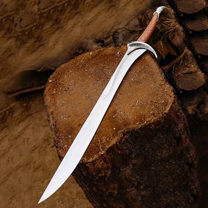 May include: A curved sword with a silver blade and a brown leather-wrapped handle. The sword is displayed on a wooden surface. The hilt is silver and the background is a textured brown wood. The overall design suggests a fantasy theme.