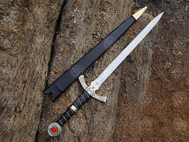 May include: An ornamental sword with a silver blade and decorative hilt, placed on a textured wooden surface. The hilt has a red gem and detailed silver patterns. A black sheath with gold accents is also present.