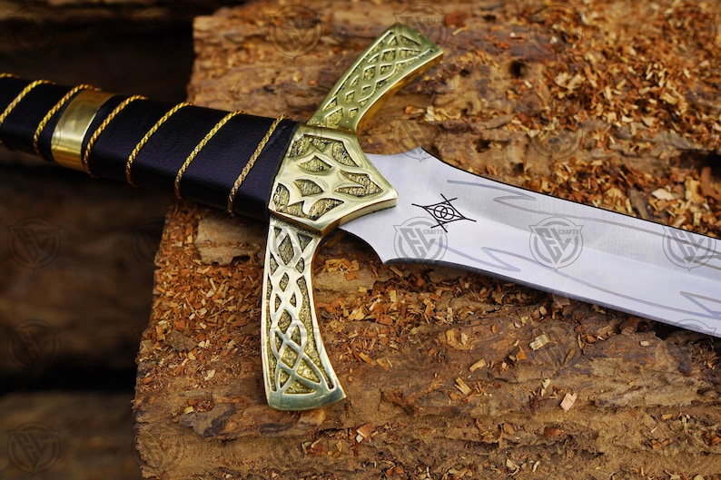May include: A detailed view of a decorative sword. The blade is silver, and the hilt is gold-coloured with intricate patterns. The handle is wrapped in black leather with gold detailing. The blade has etched designs.