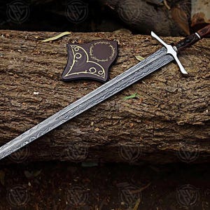 Puede incluir: Una espada larga y plateada con una hoja estampada y una guarda en forma de cruz descansa sobre un tronco. El mango es marr&oacute;n y plateado. Un parche de cuero marr&oacute;n con detalles dorados est&aacute; al lado de la espada. La espada es un art&iacute;culo de fantas&iacute;a.