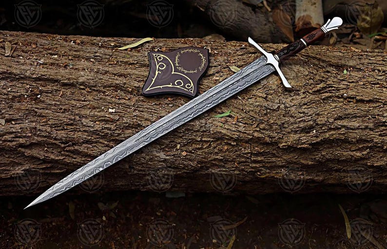 Puede incluir: Una espada larga y plateada con una hoja estampada y una guarda en forma de cruz descansa sobre un tronco. El mango es marr&oacute;n y plateado. Un parche de cuero marr&oacute;n con detalles dorados est&aacute; al lado de la espada. La espada es un art&iacute;culo de fantas&iacute;a.