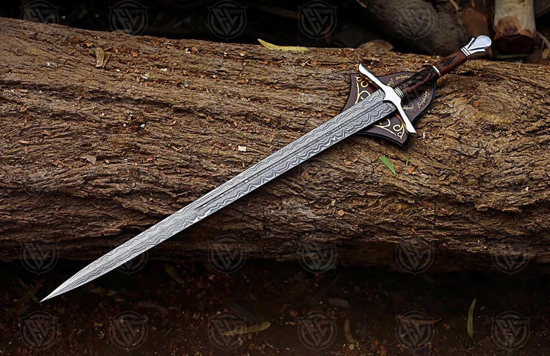 Puede incluir: Una espada larga y plateada con una hoja estampada, apoyada sobre un tronco de madera texturizado. La empu&ntilde;adura es marr&oacute;n con una guarda plateada y una placa decorativa. El dise&ntilde;o de la espada sugiere un tema hist&oacute;rico o de fantas&iacute;a.