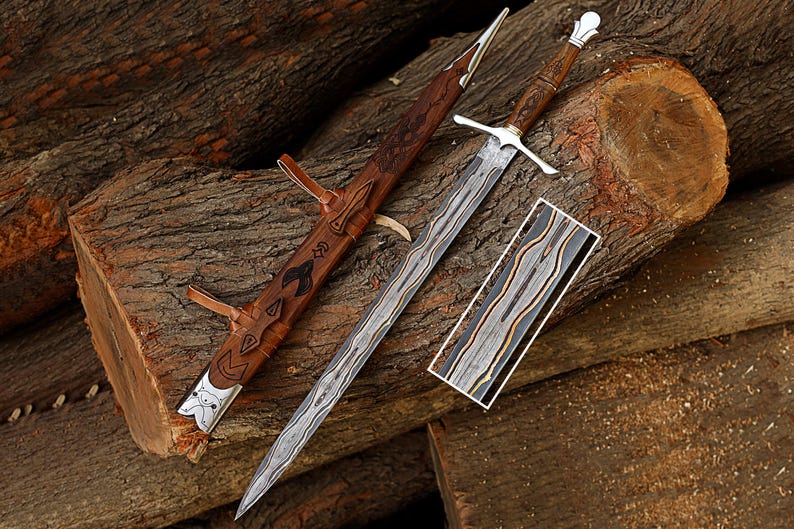 Puede incluir: Una espada artesanal con una hoja plateada y un mango de madera, apoyada sobre un tronco de madera. La espada va acompa&ntilde;ada de una vaina de cuero con grabados decorativos. Tambi&eacute;n hay una pieza rectangular de madera con un patr&oacute;n &uacute;nico.