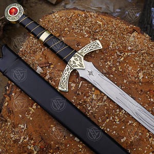 May include: A detailed image of a sword with a black handle wrapped in gold thread and a gold crossguard. The blade is silver with etched designs. The sword has a red gem at the pommel and rests in a black sheath.