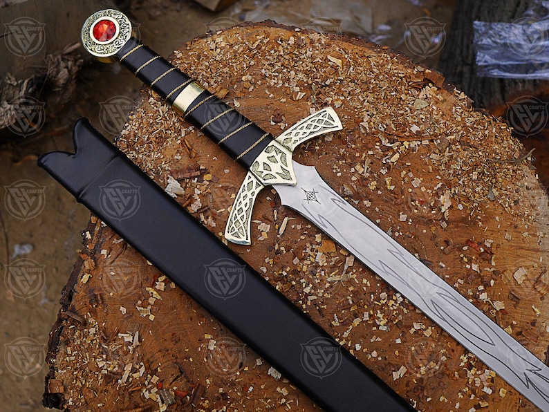May include: A detailed image of a sword with a black handle wrapped in gold thread and a gold crossguard. The blade is silver with etched designs. The sword has a red gem at the pommel and rests in a black sheath.