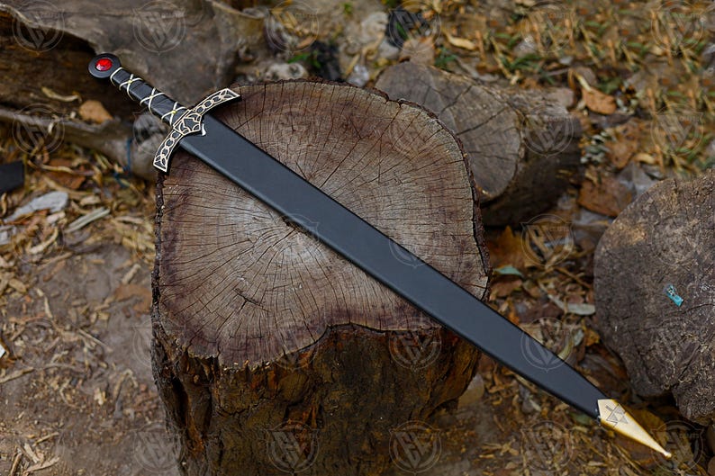 May include: A black sword with a gold and silver hilt, lying on a wooden surface. The sword has a red gem at the pommel and a decorative crossguard. The blade is black and the tip is gold.