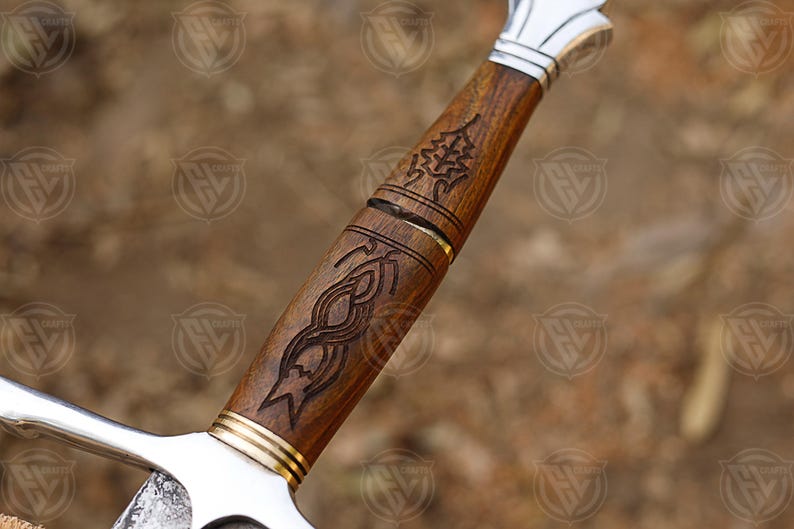 Puede incluir: Primer plano de una empu&ntilde;adura de espada con intrincadas tallas de madera. La empu&ntilde;adura es de madera marr&oacute;n oscuro con una guarda y una hoja de metal plateado. La madera presenta tallas detalladas de un &aacute;rbol y un dise&ntilde;o abstracto.