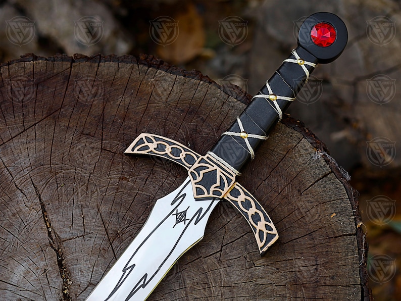 May include: A decorative sword with a silver blade and black handle. The handle is wrapped with white string and gold accents. The pommel features a red gem. The sword rests on a wooden surface.