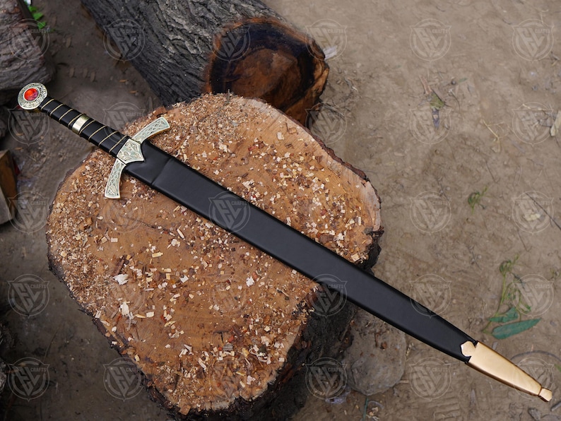 May include: A decorative sword with a black sheath, displayed on a wooden log. The sword has a gold-coloured crossguard and a red gem on the pommel. The handle is wrapped in black leather.